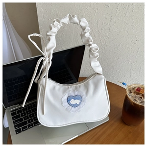 Détail du sac sous le bras en cuir blanc avec écusson lapin cœur bleu et anse plissée