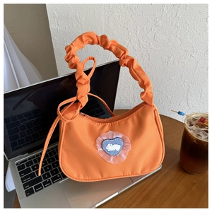 Détail du sac baguette orange avec poignée plissée et patch lapin sur un ordinateur