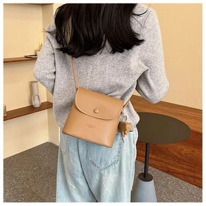 Detail of tan pebble leather crossbody bag featuring an elephant charm and thin strap