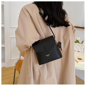 Black litchi grain bucket bag with woven shoulder strap and bear charm shown on model