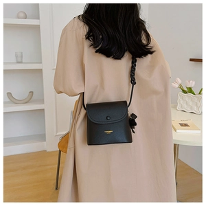 Detail of black pebbled PU leather bucket bag with woven strap and bow charm on model