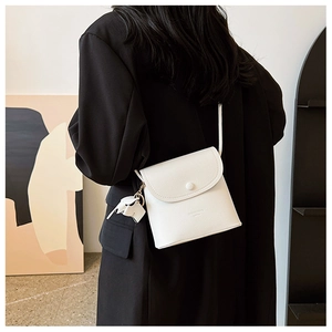 Detail of white litchi grain leather crossbody bag with cute elephant charm and round buckle