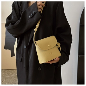 Detail of a bright yellow bucket bag with a woven shoulder strap on a black blazer