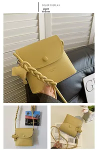 Detail of light yellow pebble grain PU leather bucket bag with woven strap and bear charm