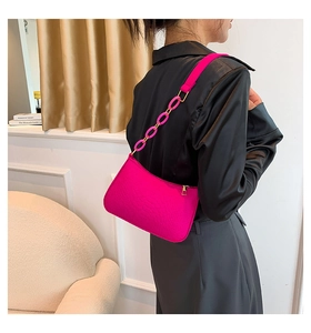 Detail of fuchsia underarm bag with crocodile embossed texture and oversized chain strap