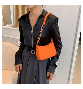 Detail of orange underarm bag showing the leather texture and gold chain strap link