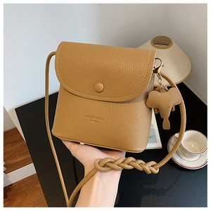 Detail of camel PU leather crossbody bag with elephant charm and woven shoulder strap
