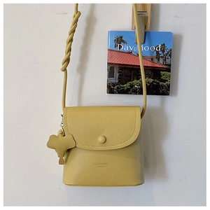 Detail of yellow lychee leather bag featuring a woven strap and cute elephant pendant