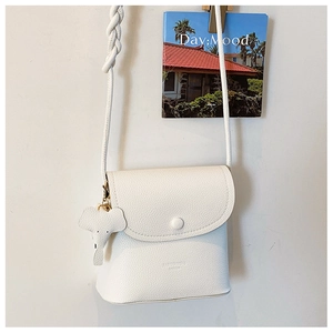 Close-up of white litchi pattern PU leather crossbody bag with braided strap and elephant charm