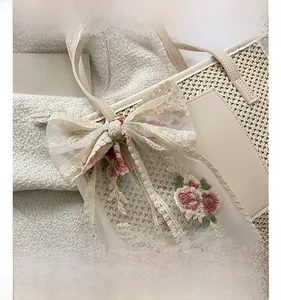 Detail of woven tote bag featuring cream lace bow and floral embroidery craftsmanship