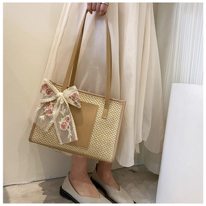 Detail of straw tote bag featuring floral lace bow and brown leather strap handle