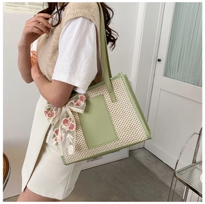 Detail of the woven tote bag featuring floral lace bow and green faux leather trim