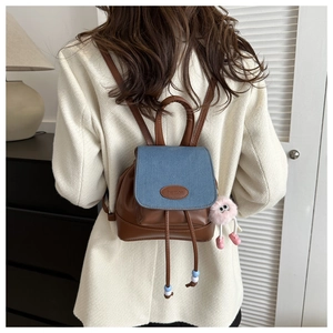 Close-up of contrast brown leather and blue denim backpack with a pink plush charm