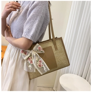 Detailed close-up of woven straw tote bag with lace bow and pink floral embroidery