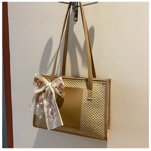 Detail of straw tote bag featuring white floral lace bow and brown leather accents