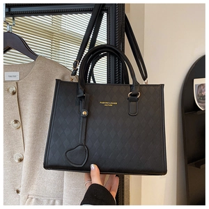 Detail of black quilted leather handbag with gold lettering and heart-shaped charm