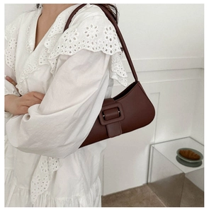 Detail of dark brown baguette bag with large square buckle on a white lace dress