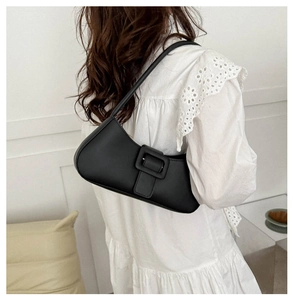 Black minimalist baguette shoulder bag with large square buckle shown on model shoulder