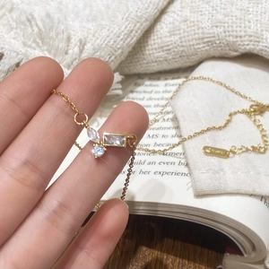 Gold plated necklace with mismatched cubic zirconia pendants held against a book background