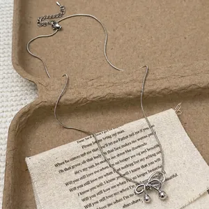 Silver bow pendant necklace with snake chain and decorative metal ball on canvas