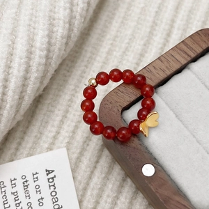 Gros plan d'une bague en perles d'agate rouge avec pendentif papillon doré sur support