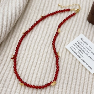 Détail d'un collier en perles d'agate rouge avec breloques papillon dorées sur tricot