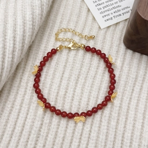 Gros plan d'un bracelet en perles d'agate rouge avec des breloques papillon dorées
