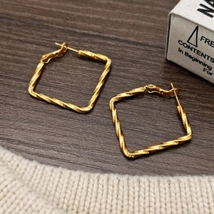 Vintage gold square twist hoop earrings with textured metal finish on a rustic wood background