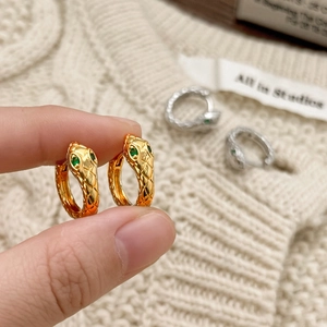Chic gold snake hoop earrings with green zircon eyes and textured scales on beige knit