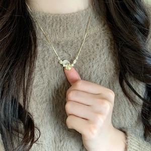 Elegant gold necklace with clover and cat's eye stone pendant worn on a brown sweater