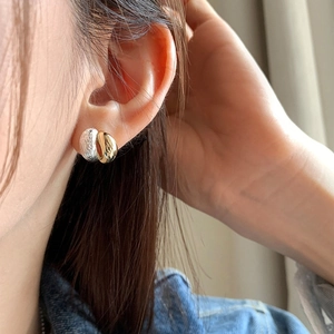 Close-up of two-tone metal earrings with brushed silver and polished gold finish