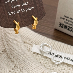Knot design hoop earrings in gold and silver finish on a textured lifestyle background