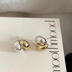 Detail of two-tone metal stud earrings featuring matte silver and polished gold textures