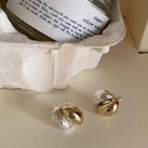 Detail of mixed-metal oval earrings featuring polished gold and brushed silver textures