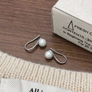 Elegant pearl earrings with S-shaped silver hooks on a rustic wooden background