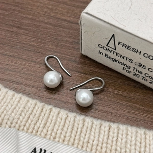 Elegant white pearl hook earrings with polished silver metal on soft knit background
