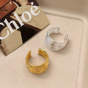 Detailed view of layered spiral gold and silver geometric rings on a beige surface