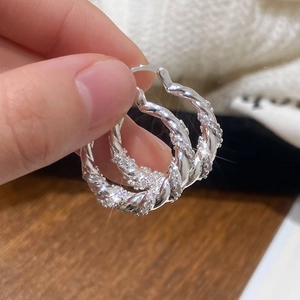 Silver twisted hoop earrings with zircon pavé setting shown in a hand-held macro shot