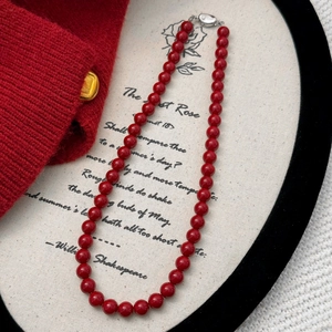 Macro view of vintage red beaded necklace with silver clasp on white fabric surface