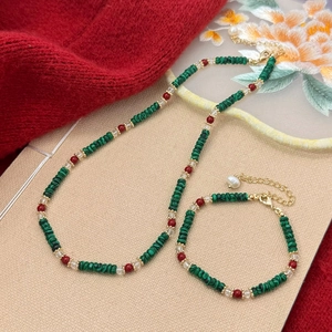 Handmade jewelry set with green stone beads, red accents and pearl drops on a textured background