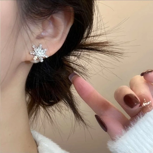 Minimalist snowflake stud earrings with zircon and pearls worn on a model's ear