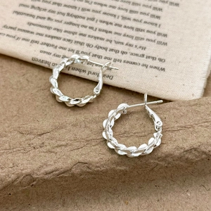 Silver twisted hoop earrings with a textured weave design on artistic canvas background