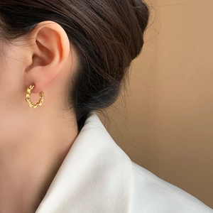 Minimalist gold twisted rope hoop earrings with shiny metallic finish worn by female model