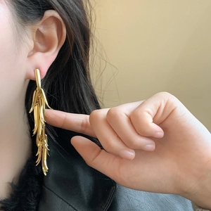 Eleganti orecchini lunghi a nappa dorati con design a spiga su modella in pelle nera