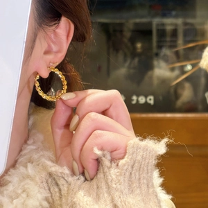 Fashionable gold twisted rope textured large hoop earrings worn by a model