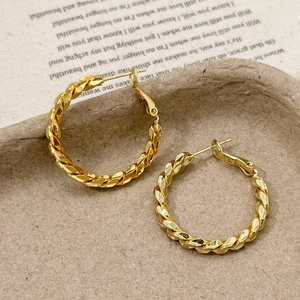 Close-up of golden twisted hoop earrings with textured finish on vintage book paper