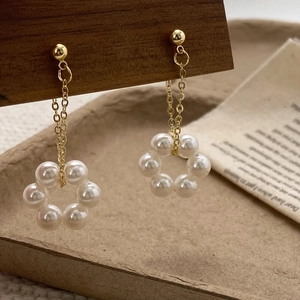 Detail of elegant gold chain earrings with pearl flower pendant on a wooden stand