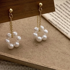 Detail of elegant gold chain earrings with circular pearl flower wreath on a vintage paper