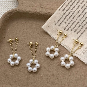 Close-up of elegant gold pearl wreath tassel earrings on a textured paper tray