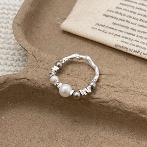 Macro detail of elastic pearl and silver bead ring on a textured brown display tray